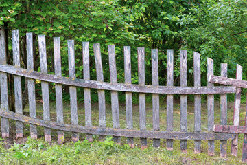 An old, leaning wooden fence against the background of the forest. The fence has been repaired many times, but it's time to throw it away.