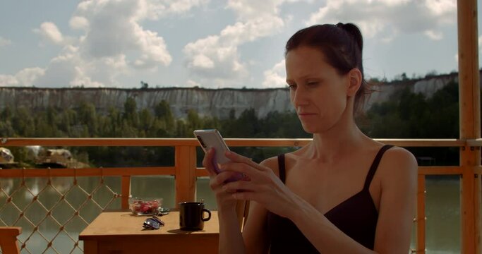 Female comunicate by smartphone with friends while resting on lake on weekend