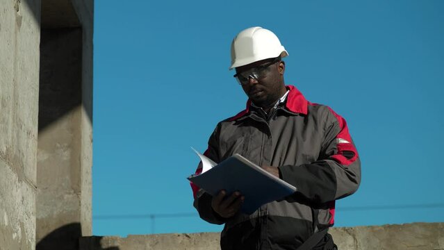 African american workman stands at construction site, holds in hands work papers and looks around