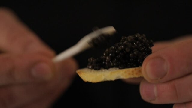 Spoon with black caviar in man hand. Luxurious delicacy. The cook makes sandwiches with black caviar.
