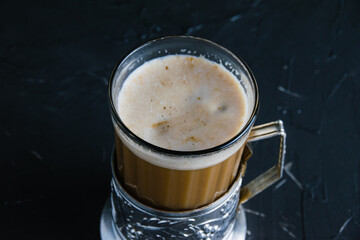 Aromatic cappuccino coffee in a glass cup with a vintage coaster on a dark concrete background with copy space.