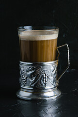 Aromatic cappuccino coffee in a glass cup with a vintage coaster on a dark concrete background with copy space.