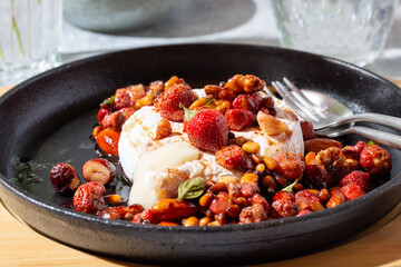 Baked camembert cheese served with berries, nuts and herbs sauce on gray table on sunny day. Close-up.