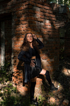 beautiful woman in black stockings and a black skirt in the woods near a brick wall