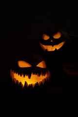 Two Halloween pumpkins smile with scary eyes for party night. Close up view of scary Halloween pumpkin with eyes glowing inside at black background. Selective focus