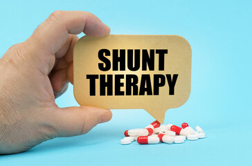 On a blue surface are pills in a persons hand, a sign with the inscription - Shunt Therapy