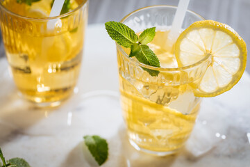 Ice tea with lemon and mint leaves. Served with ice on marble background. Summer refreshing cocktail drink