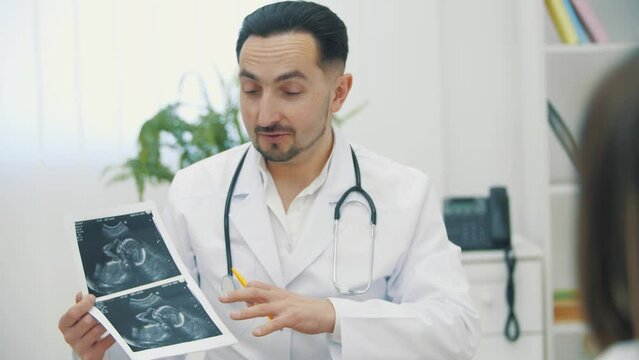 4k slow motion video of doctor wearing white lab coat holding ultrasound photos and explaining.