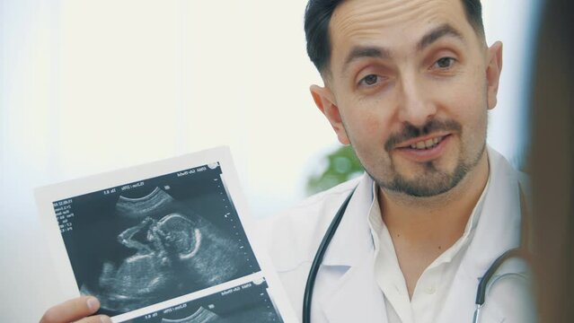 4k slow motion video of doctor wearing white lab coat holding ultrasound photos and explaining.