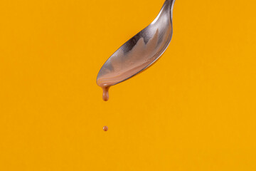 Colher derrubando sorvete de chocolate e gota flutuando sobre fundo amarelo