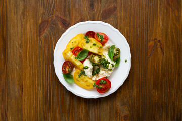 Top view of summer tomato salad with cheese and pesto on wooden surface