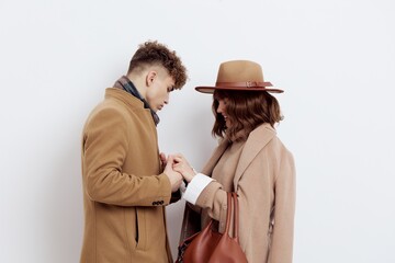 a beautiful, pleasant couple, a man and a woman stand on a light background gently holding hands, dressed in warm brown autumn coats. Horizontal studio photography with empty space