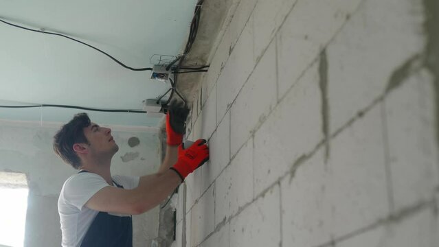Electrician mounting junction box, instaling electrical wiring in apartment. Repairman feeds wires, cable into electrical box. Repair and construction work. Contractor working on apartment renovation.