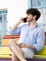 Young smiling man sitting on a bench talking on the smartphone