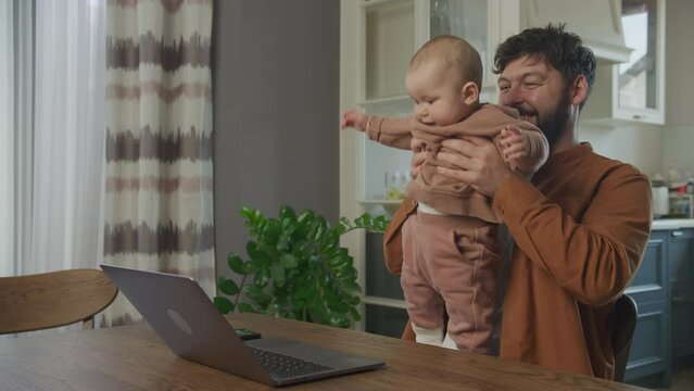 Young father hold his baby boy video calling on laptop computer
