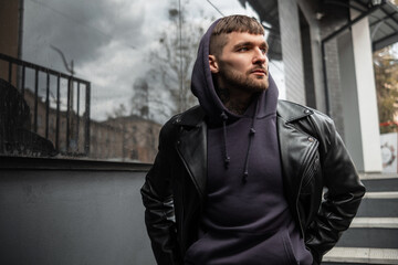 Cool stylish handsome man model in fashionable street clothes with leather jacket and hoodie...