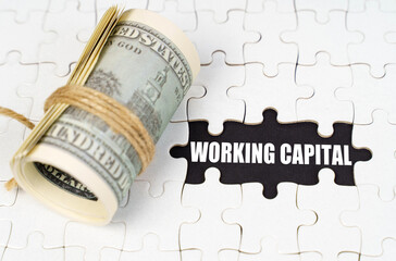 Dollars lie on white puzzles, on a black surface there is an inscription - Working Capital