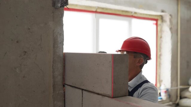 Contractor applies polyurethane foam adhesive with a gun nozle on concrete wall to glue autoclaved aerated concrete brick. Worker sprays the PU foam. Isolated view.