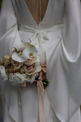 young girl in a white wedding dress holds in her hands a bouquet of flowers and greenery 