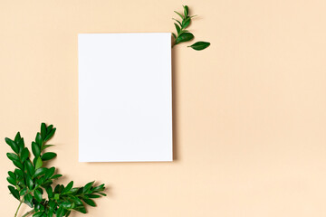 Rectangular vertical or square invitation white greeting card mockup with a boxwood branch. Top view with copy space, pastel light yellow beige background. Template for branding and advertising