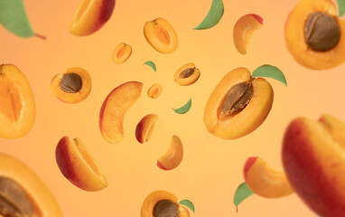 Close up studio macro photo of half and sliced ripe floating apricots on orange yellow background.