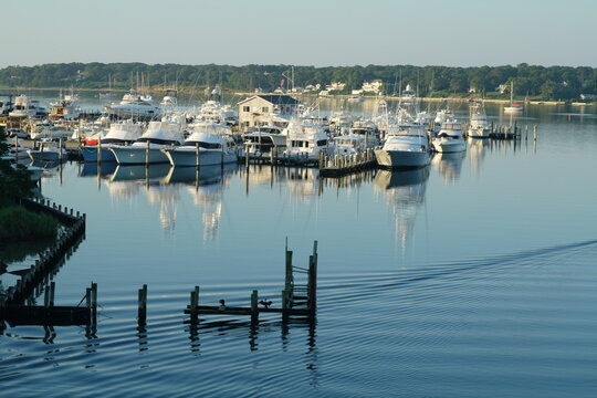 Boats in Hamptons marina with calm water and mirror reflection on summer morning