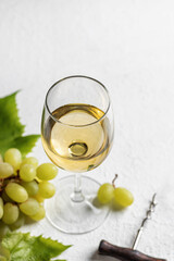 Glass of white wine on white background with corkscrew and grapes, text space