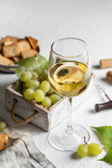 Glass of white wine on white background with corkscrew and cork, grapes and crackers