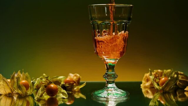 Close up of pouring fruit drink inside an empty glass. Stock clip. Bar counter decorated by small yellow berries on the background of a wall with changing lights.