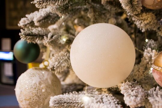 White decorative ball on the christmas tree on glitter bokeh background with blurred snow. Merry christmas card. Winter xmas theme. Happy New Year. Snowing.