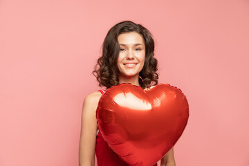 Fototapeta na wymiar Portrait of young lady stands on pink background with heart shapped decoration