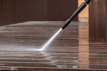 Man cleaning walls and floor with high pressure power washer. Washing terrace wood planks and...