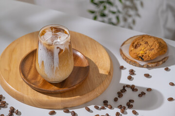 Glass of a brewing iced coffee with creamy milk and served with cookies. Cold coffee drink glass with ice and cream milk on white table.
