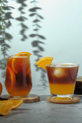 cold Iced black coffee mixed with orange juice and orange slices in glass on wooden plate in white background with nature leaves silhouette shadow. two tones layer fresh summer drink in the morning