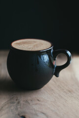 Coffee latte in black ceramic cup on wooden table in cafe with dark background