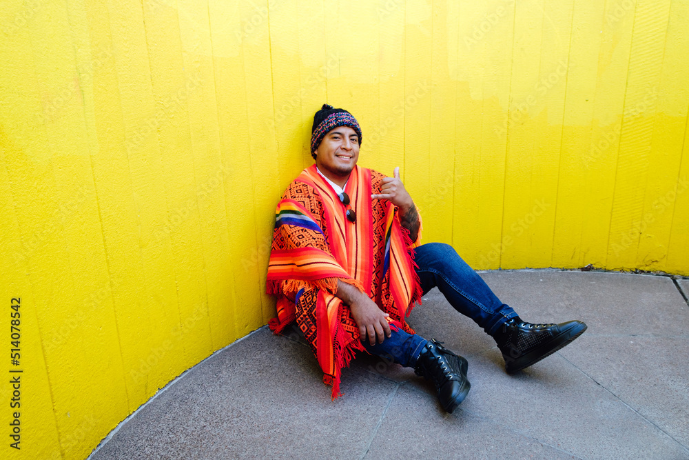 Sticker Young man with peruvian colorful poncho sitting in front of yellow wall