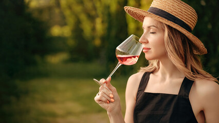 a woman in a straw hat tastes or smells rose wine at a winery