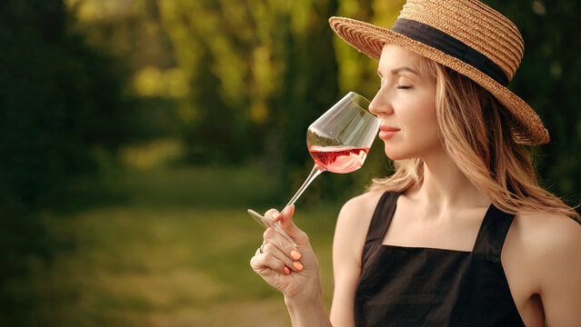 A Woman In A Straw Hat Tastes Or Smells Rose Wine At A Winery