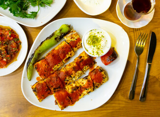 Plate of delicious beyti kebab, traditional Turkish dish of minced lamb grilled on skewer and wrapped in lavash topped with tomato sauce served with baked vegetables and yogurt