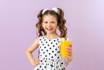 A glass of orange juice in the child's hands. A little girl in a polka dot dress holds citrus juice...