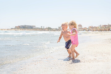 happy children laugh run play on waves on beach by sea