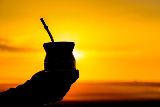 Silhouette of a hand holding a yerba mate drink at golden sunset