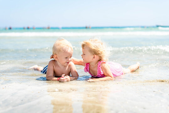 little girl hugs boy lie on beach in sea in ocean