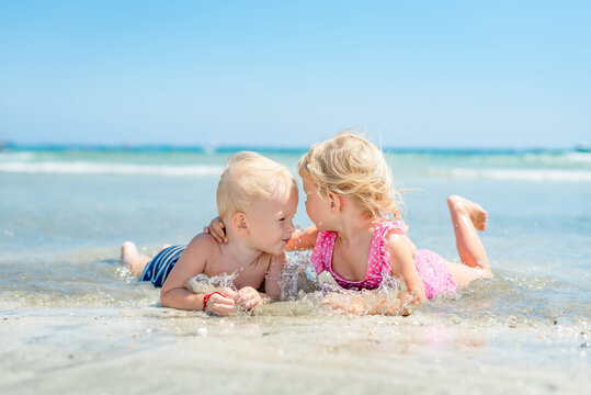 little girl hugging boy lying on beach in sea in ocean