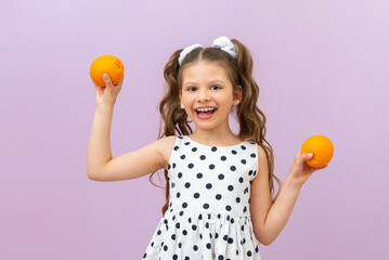 A little girl holds oranges in her hands and smiles broadly on a pink isolated background.  Citrus fruits for baby food.