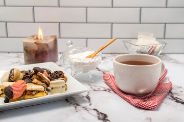 breakfast or snack with a cup of tea fine doughs of cornstarch chocolate vanilla and dulce de leche on a marble table with sugar bowl and decorative candle