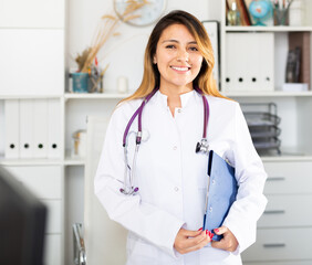 Young mexican female medic in uniform holding clipboard in doctor's office