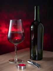 A bottle of red wine and a glass and a corkscrew against a dark background