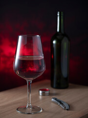A bottle of red wine and a glass and a corkscrew against a dark background