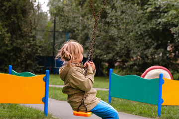 A cheerful girl of 10 years old is swinging on a swing in the playground. A child plays outside in...